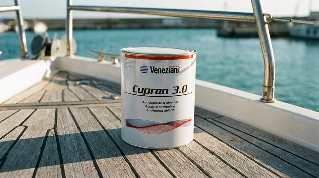 Barattolo di antivegetativa Veneziani Cupron 3.0 sul ponte in teak di una barca a vela in cantiere, con il mare sfocato sullo sfondo
