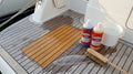 Coperta in teak durante la pulizia: un riquadro già pulito color miele accanto alle doghe grigie, con i flaconi Teak Wonder Cleaner e Brightener, un secchio e uno spazzolone