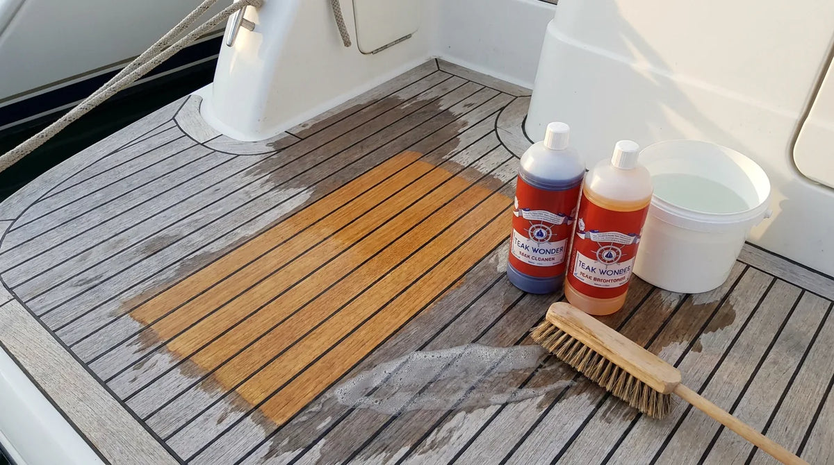 Coperta in teak durante la pulizia: un riquadro già pulito color miele accanto alle doghe grigie, con i flaconi Teak Wonder Cleaner e Brightener, un secchio e uno spazzolone