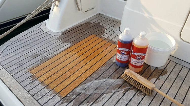 Coperta in teak durante la pulizia: un riquadro già pulito color miele accanto alle doghe grigie, con i flaconi Teak Wonder Cleaner e Brightener, un secchio e uno spazzolone
