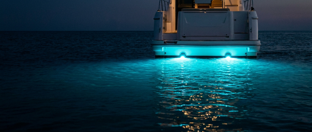 Due luci LED subacquee accese sullo specchio di poppa di una barca, con alone turchese nell'acqua di notte