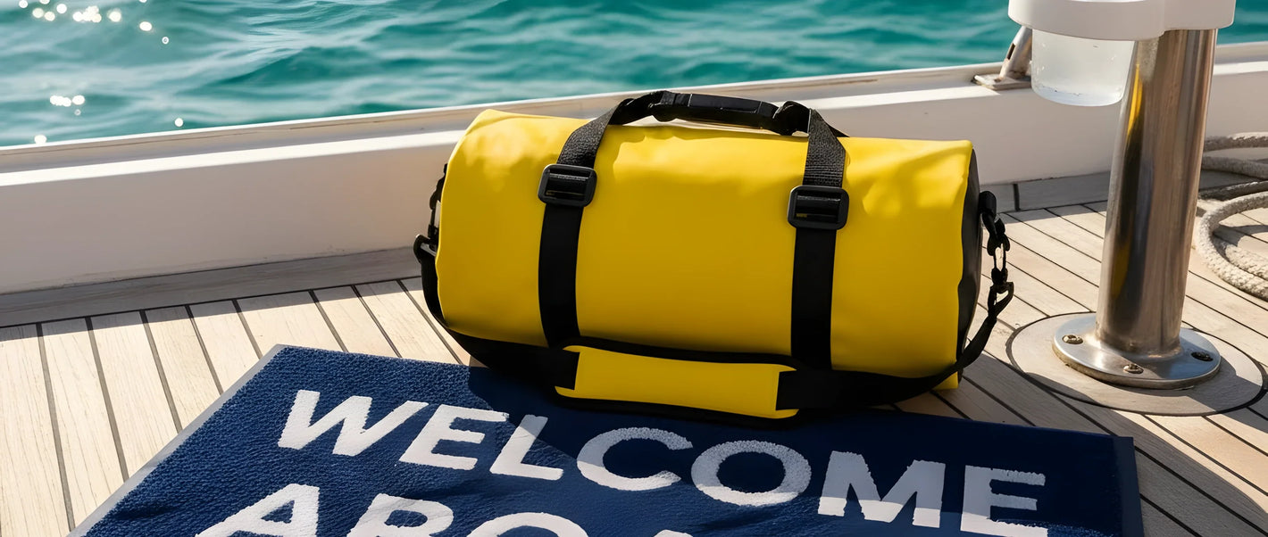Una composizione sul ponte di una barca: una sacca stagna colorata, uno zerbino "Welcome Aboard" e un portabicchieri installato con un bicchiere dentro.