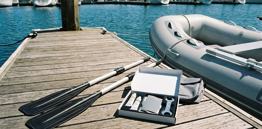 Accessori per tender e gommoni appoggiati su un pontile di legno, inclusi remi in alluminio, kit di riparazione con colla e toppe, e una sacca portaoggetti vicino al tubolare del gommone.