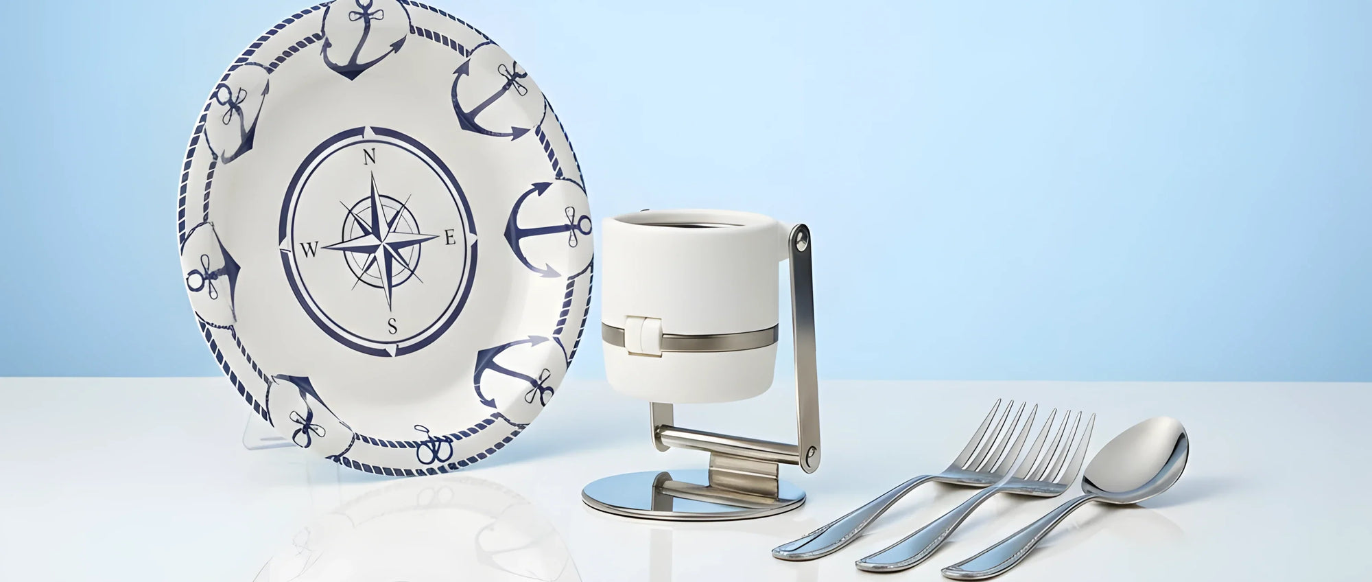 Un set di accessori misti: un portabicchieri bianco pieghevole, un piatto in melamina con decoro nautico e una sessola arancione per l'acqua.