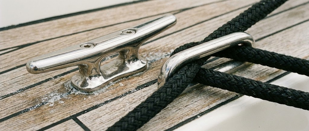 Una bitta a galloccia in acciaio inox lucidato a specchio montata su una coperta in teak, con una cima da ormeggio nera passata attraverso un passacavi.