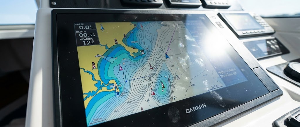 Primo piano dello schermo di un GPS Plotter Garmin acceso che mostra una carta nautica dettagliata con linee batimetriche, colori dei fondali e la rotta tracciata.