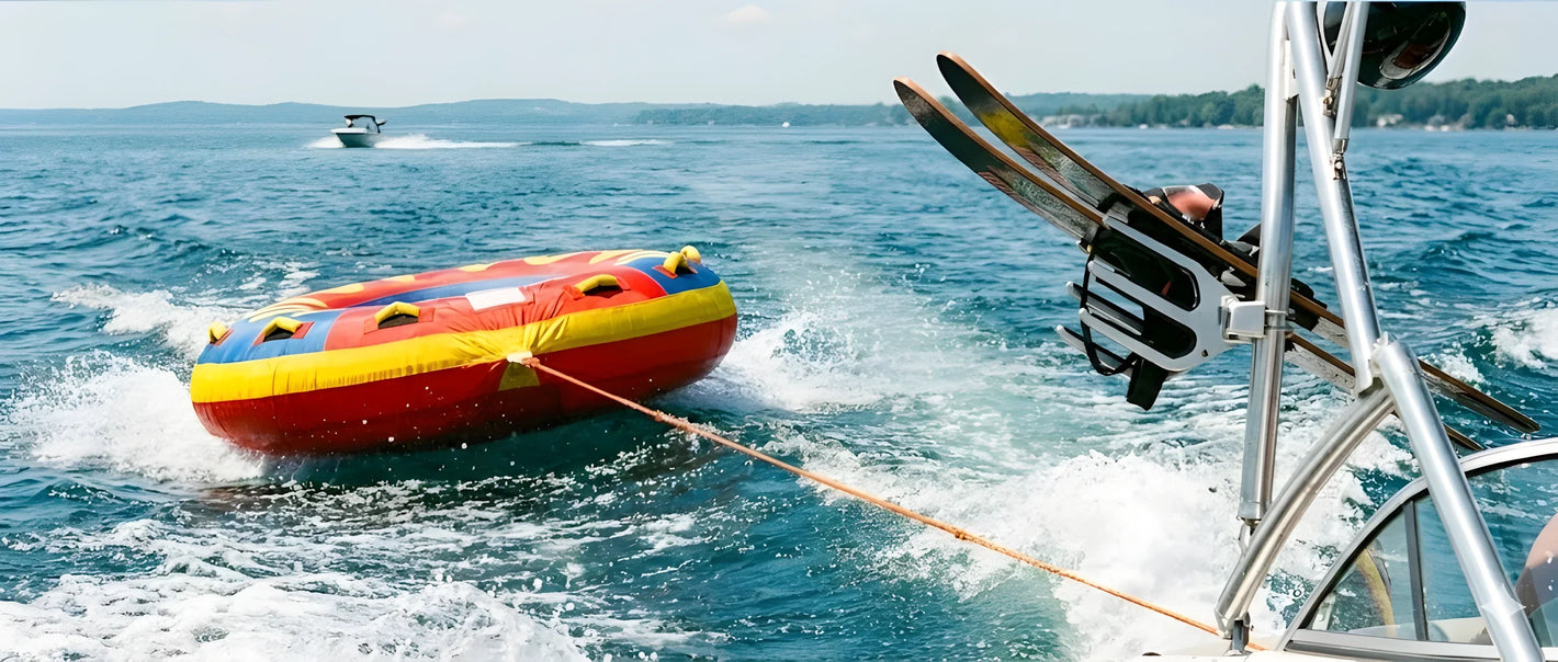 Una composizione dinamica con una ciambella trainabile colorata (gialla e rossa), un paio di sci nautici e una cima da traino galleggiante arancione.