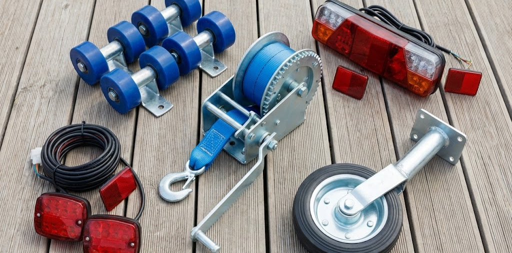 Assortimento di ricambi per carrelli nautici inclusi argano manuale, kit luci posteriori, rulli centrali e ruotino di manovra.