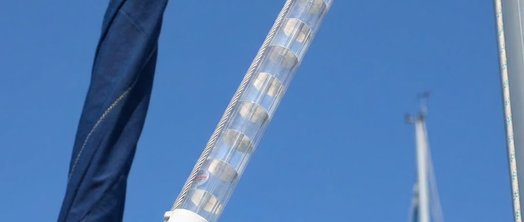 Vista dal basso verso l'alto dell'albero di una barca a vela: un riflettore radar tubolare bianco è installato su una sartia contro il cielo azzurro.