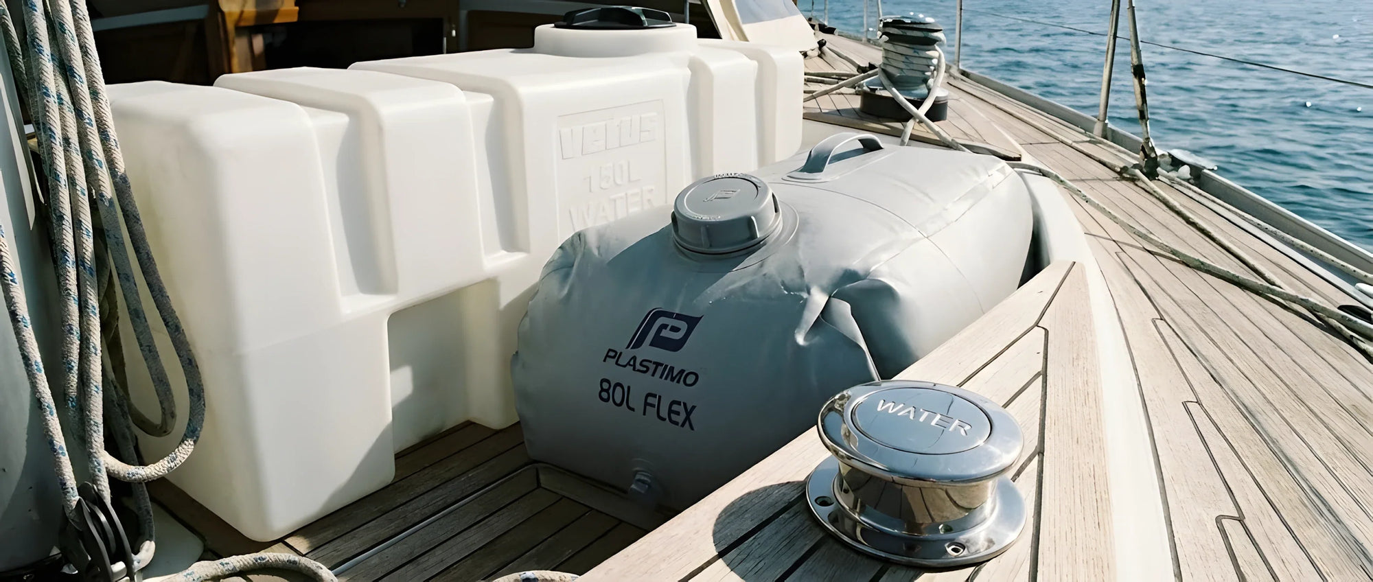 Un serbatoio rigido bianco in polietilene accanto a un serbatoio flessibile grigio (a sacca) riempito, con un tappo d'imbarco "Water" in primo piano.