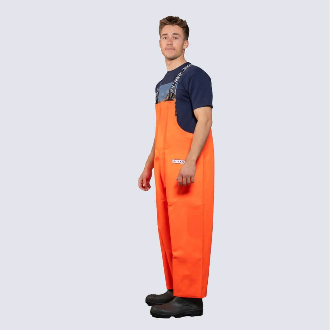 Salopette nautica Ocean® Mariner arancione impermeabile con bretelle, vista laterale, indossata con stivali neri | Onautica